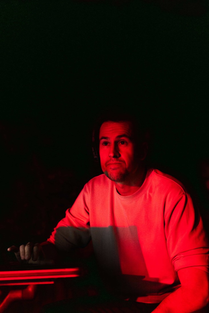 Héctor con auriculares escribiendo frente al portátil bajo luz roja